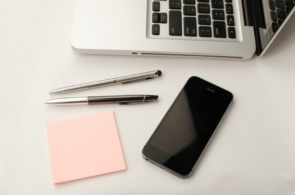 pexels-photo-296116-296116 Clean and modern workspace featuring a laptop, smartphone, pens, and sticky notes.
