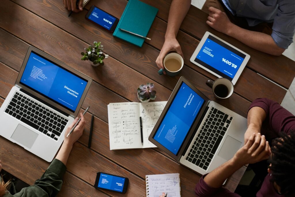 pexels-photo-3183190-3183190 Top view of a diverse team using technology in a meeting. Laptops, tablets, and smartphones on a wooden table.