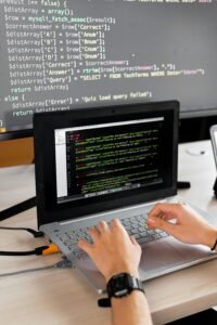 Person coding at a desk with laptop and external monitor showing programming code.